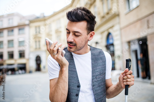 Slika na platnu Young blind man with smartphone on street in city, making phone call