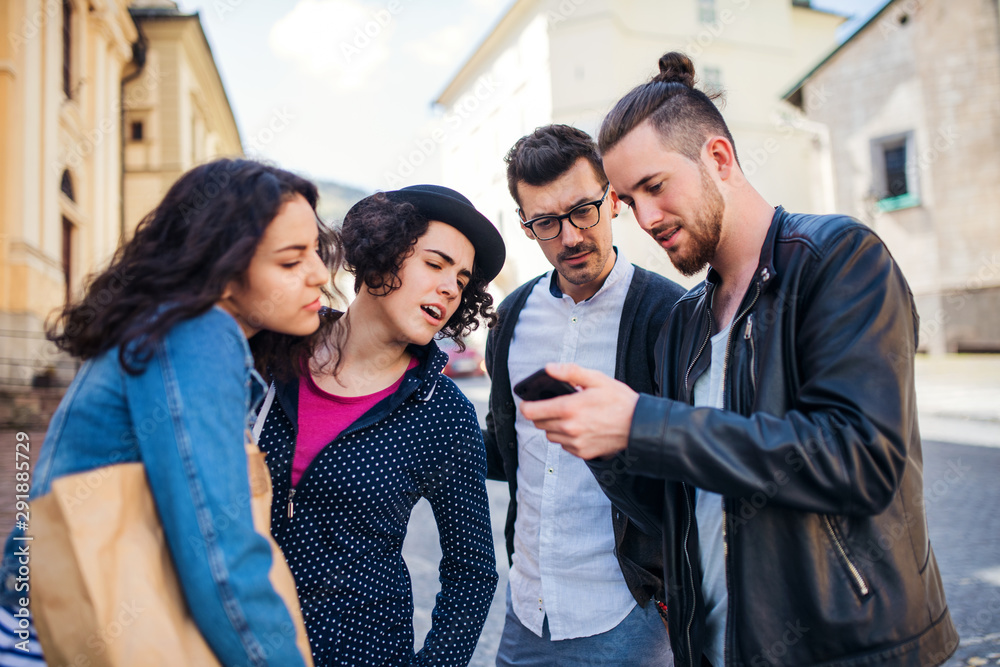 A group of young friends standing outdoor in town, using smartpone. A group of young friends standing outdoor in town, using smartpone.
