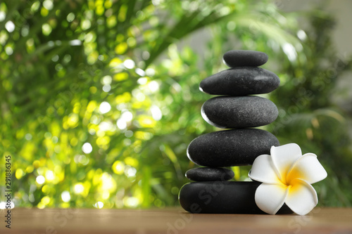 Table with stack of stones  flower and blurred green leaves on background  space for text. Zen concept