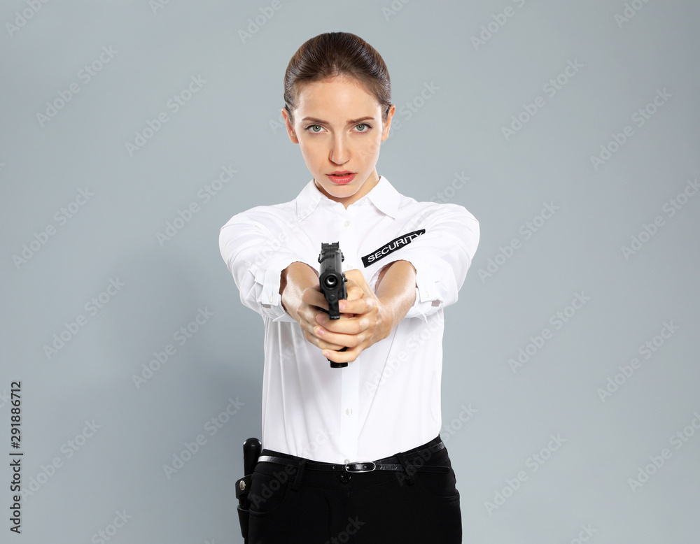 Female security guard in uniform with gun on grey background Female security guard in uniform with gun on grey background