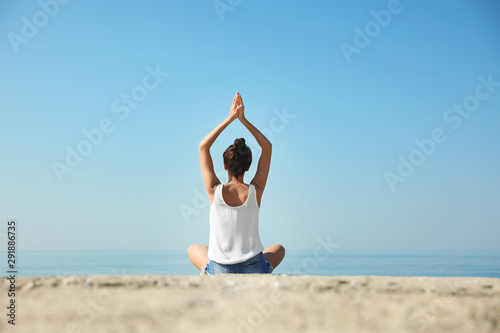 Beautiful young woman practicing yoga near sea