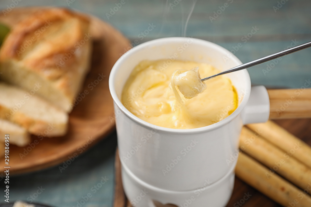 Pot of tasty cheese fondue and fork with bread on blue wooden table Pot of tasty cheese fondue and fork with bread on blue wooden table