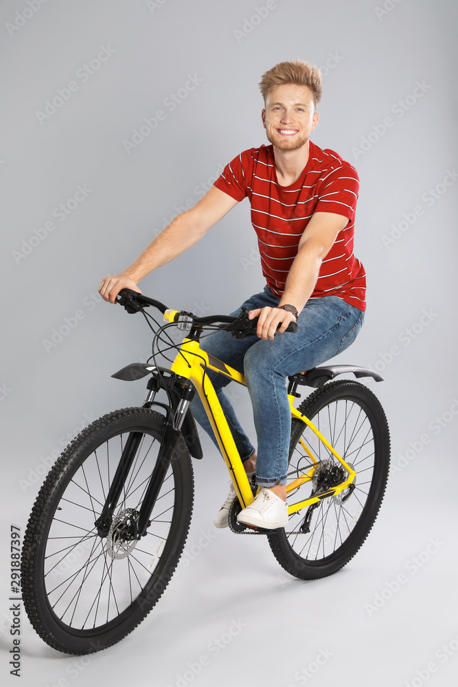 Handsome young man riding bicycle on grey background Handsome young man riding bicycle on grey background