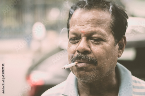 Portrait of a A mid adult senior mature man of Asian and Indian Ethnicity is smoking cigarette. Front View. Close up. Photography taken on 31 May 2019 on World No Tobacco or anti Tobacco Day