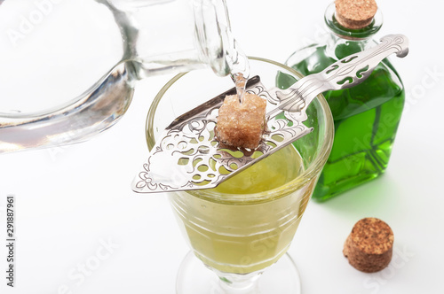 Obraz na płótnie Alcohol, luxurious spirits and dangerous liquor conceptual idea with crystal glass of absinthe, pouring water on stainless steel spoon, sugar cube and green bottle of strong spirit on white background w salonie