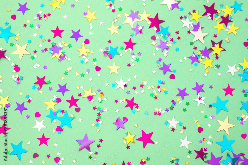 Colorful foil stars confetti sparse on trendy mint colored background. Simple holiday texture. Top view, flat lay Colorful foil stars confetti sparse on trendy mint colored background. Simple holiday texture. Top view, flat lay