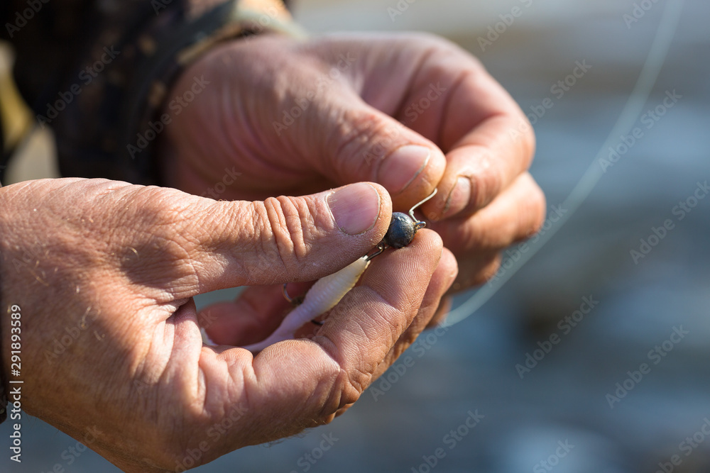 Angler tying a fishing hook to rubber worm lure. Fishing for larva spinning on a lake. Angler tying a fishing hook to rubber worm lure. Fishing for larva spinning on a lake.
