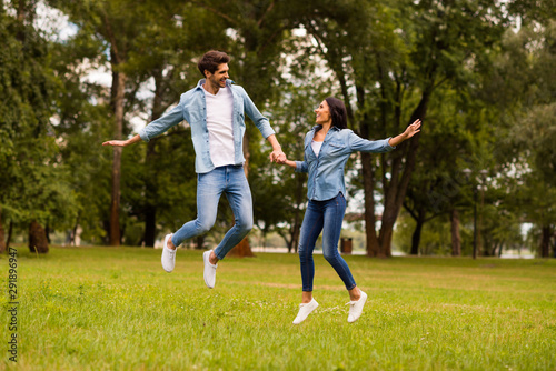 Full body photo of cute pair holding hands jumping high in green park wear denim outfit