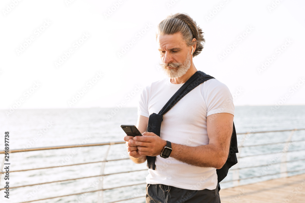 Image of thinking old man using earpod and cellphone while working out