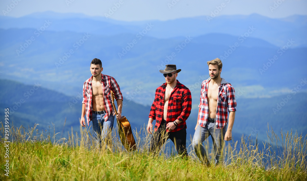 Tourists hiking concept. Enjoying freedom together. Group of young people in checkered shirts walking together on top of mountain. Hiking with friends. Friendly guys with guitar hiking on sunny day