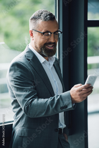handsome businessman in formal wear and glasses holding smartphone