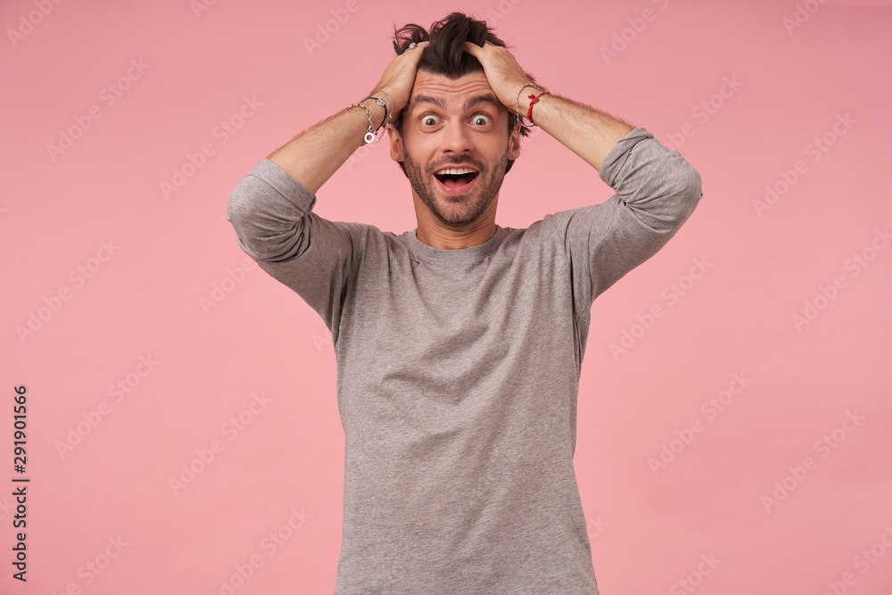 Studio photo of beautiful amazed bearded male with trendy haircut wearing casual clothes, posing over pink background with hands on his head, looking at camera with dazed face and wide mouth opened Studio photo of beautiful amazed bearded male with trendy haircut wearing casual clothes, posing over pink background with hands on his head, looking at camera with dazed face and wide mouth opened