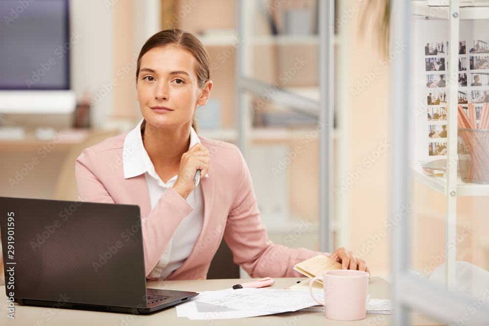 Portrait of young office manager sitting at the table in front of laptop and working with documents Portrait of young office manager sitting at the table in front of laptop and working with documents