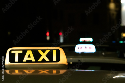 Taxi roof advertising signs lit up on taxi cars waiting in a taxi station.