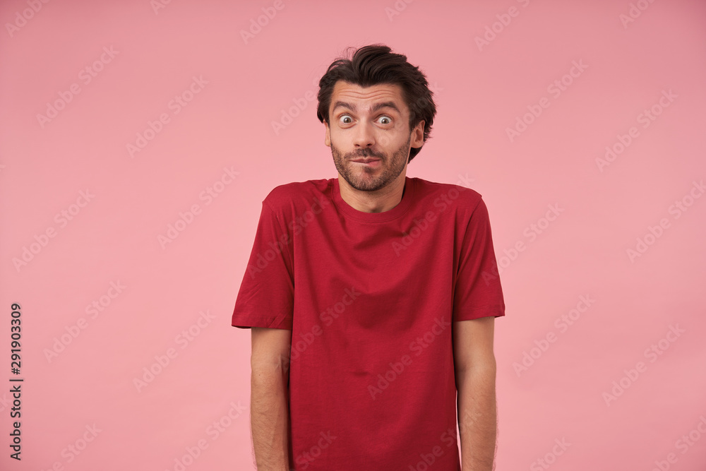 Positive young man with trendy haircut wearing red t-shirt, standing over pink background with hands down, looking at camera with wide eyes opened, contracting forehead and raising eyebrows Positive young man with trendy haircut wearing red t-shirt, standing over pink background with hands down, looking at camera with wide eyes opened, contracting forehead and raising eyebrows