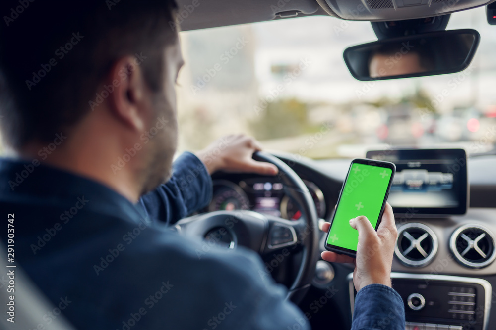 Photo from back of man with phone with green screen in his hands at wheel of car Photo from back of man with phone with green screen in his hands at wheel of car