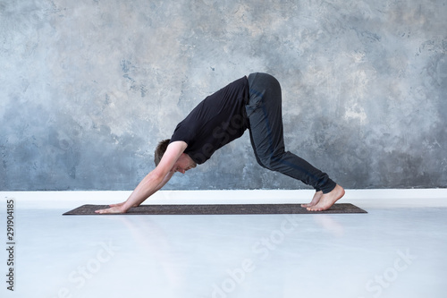 Fototapeta Young man working out, standing in yoga downward facing dog pose