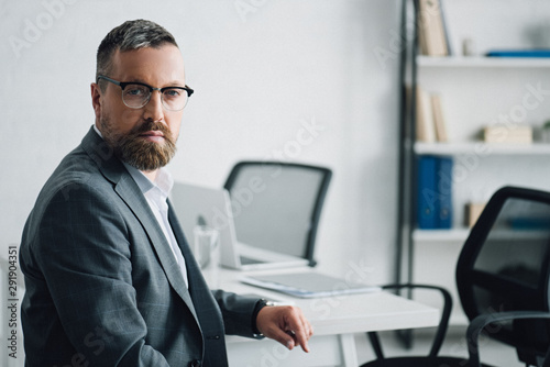 handsome businessman in formal wear and glasses looking at camera in office