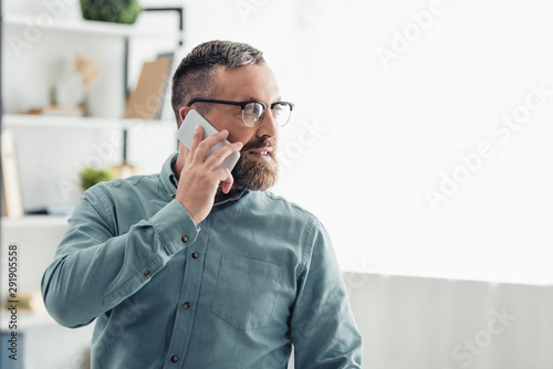handsome businessman in shirt talking on smartphone and looking away