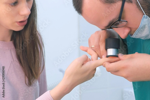 Surgeon and patient woman examine wart on finger of using dermatoscope magnifier before laser removing. Inspecting verruca on hand, cure and treatment. One day surgery concept.