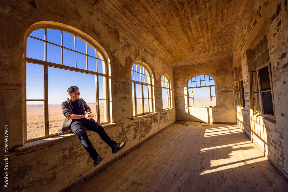 Tourist sits in a widow of a ruined house in Kolmanskop ghost town, Namibia Tourist sits in a widow of a ruined house in Kolmanskop ghost town, Namibia