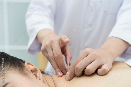 doctor or Acupuncturist inserting a needle into Asian female neck or back. patient having traditional Chinese treatment using acupuncture to restore an energy flow through specific points on the skin