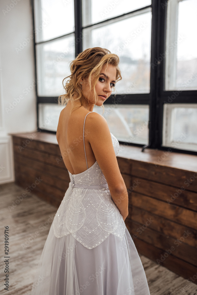 the bride in a beautiful dress stands at the window in the white Studio the bride in a beautiful dress stands at the window in the white Studio