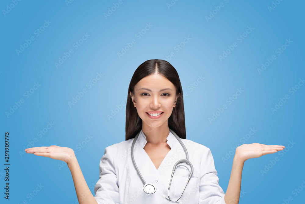 A young Asian woman doctor is scaling with her arms two different options in front of isolated and easy to remove blue background. Communicate about healthcare health and medical choices or compare A young Asian woman doctor is scaling with her arms two different options in front of isolated and easy to remove blue background. Communicate about healthcare health and medical choices or compare