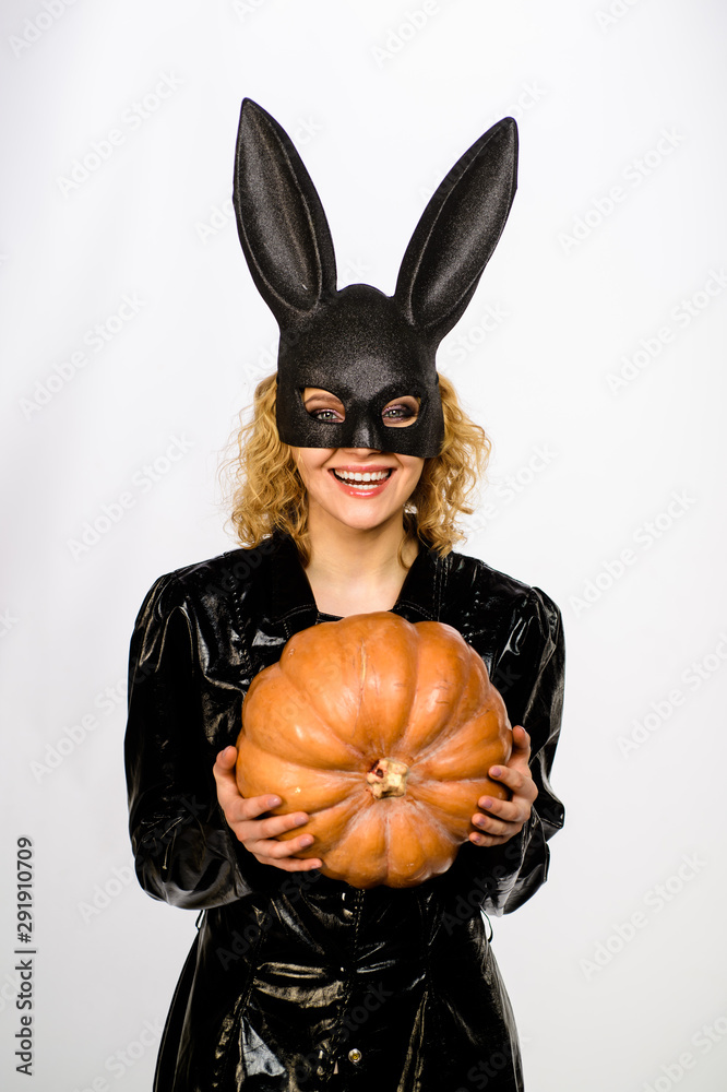 Beautiful girl in halloween bunny costume holds pumpkin. Sexy blonde woman  in rabbit black mask with pumpkin. Sexy female model in Easter bunny black  rabbit mask with jack-o-lantern. Happy Halloween. Stock Photo