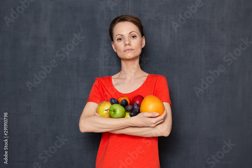 Portrait of serious woman holding ripe fresh fruits in hands