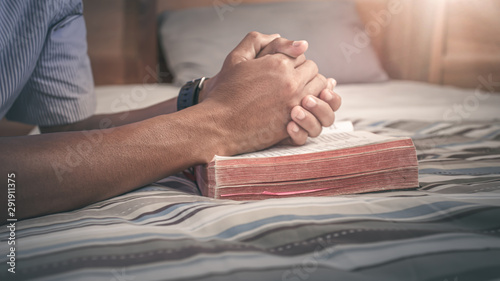 Close up holy Bible with hands of young man praying on the bed. christian praying concept.