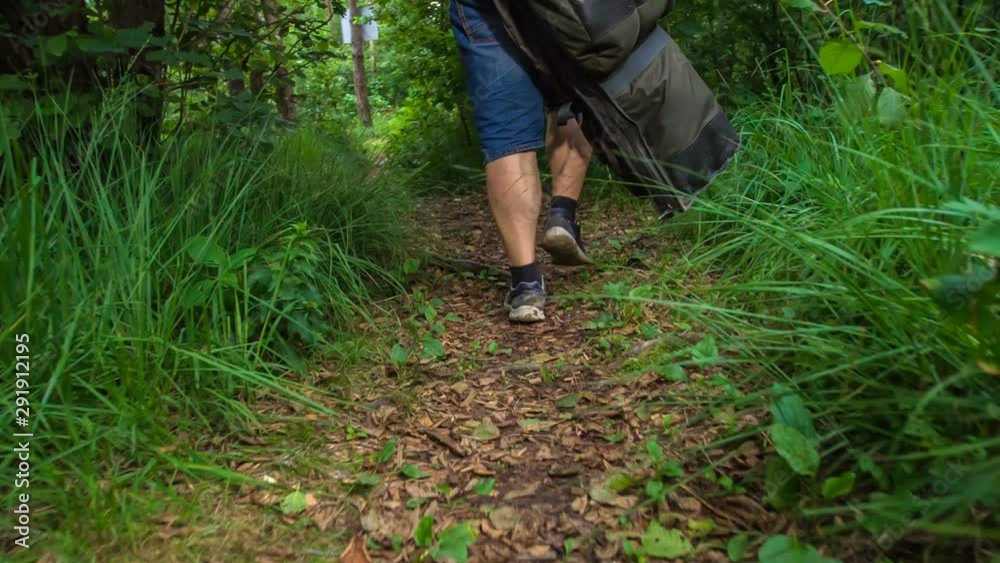 A fisherman is walking on a forest path. The grass is beautiful and green. A fisherman is walking on a forest path. The grass is beautiful and green.