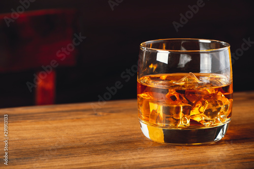 Whiskey with ice cubes in glasses on a wooden tabletop in a pub, dark background, copy space.