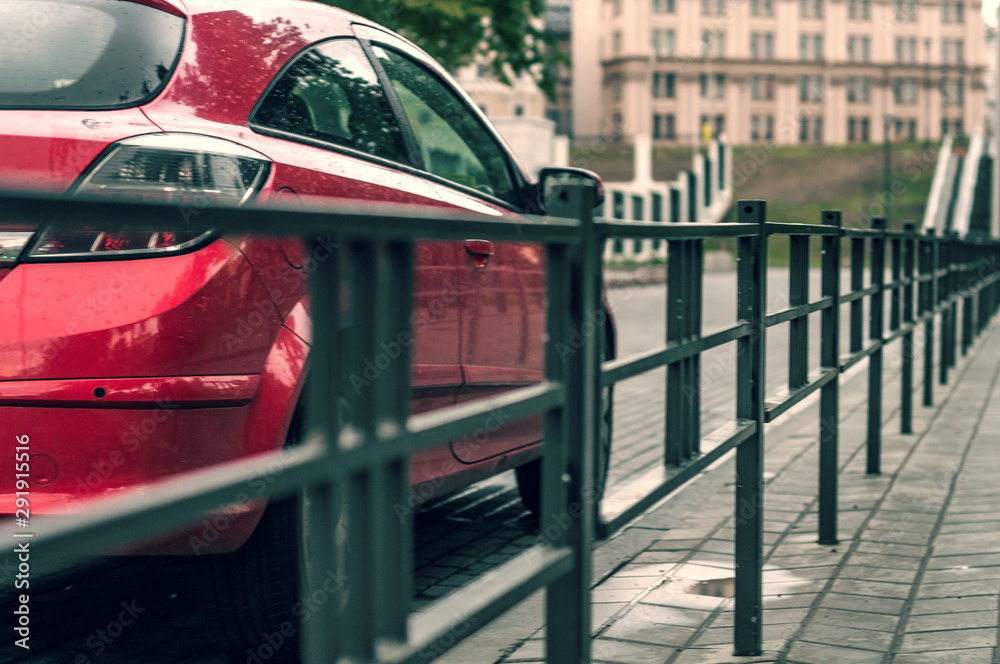 Fototapeta premium parked red car at the iron fence