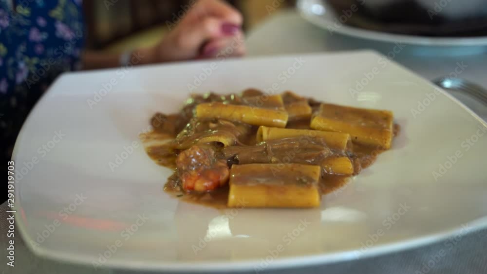 Close-up of woman's hand sitting in luxury restaurant, holding fork and tasting delicious italian pasta with mushroom sauce and shrimps. Italian tasty cuisine in restaurant. Italian short pasta for Close-up of woman's hand sitting in luxury restaurant, holding fork and tasting delicious italian pasta with mushroom sauce and shrimps. Italian tasty cuisine in restaurant. Italian short pasta for