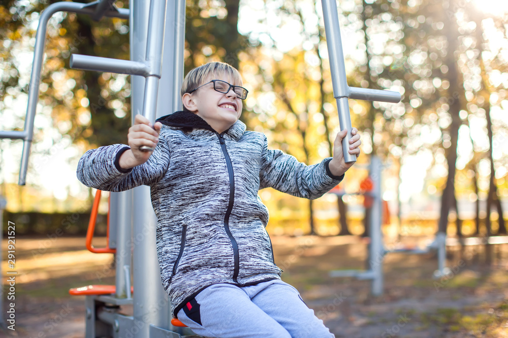 Obraz premium Smart kid boy does workout on trainer equipment outdoor. Children, sport, activity and healthcare concept