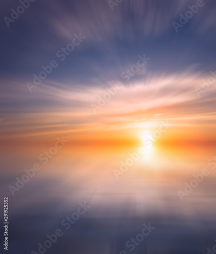 Bright sunset with rays on the background of soft clouds over the sea.