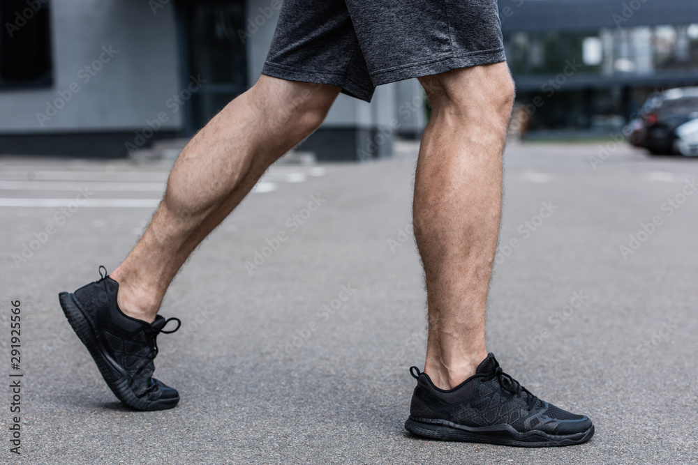 partial view of sportsman in black sneakers walking on street