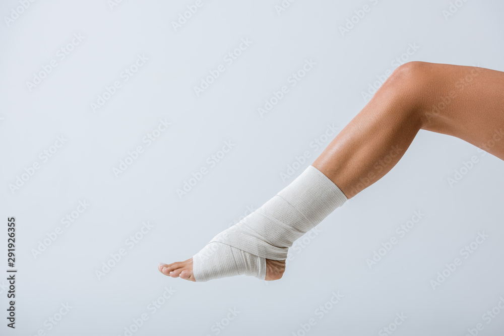 partial view of barefoot girl with elastic bandage on foot isolated on grey