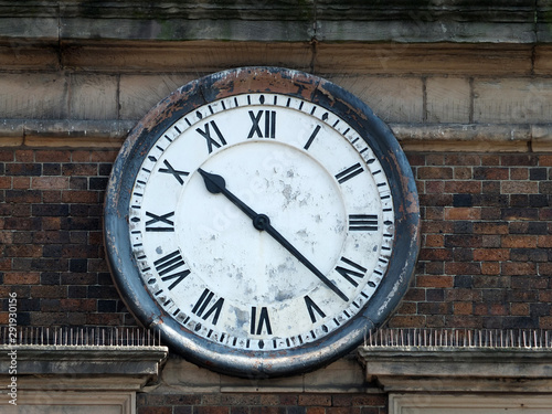 old round clock on the brick wall of a building with roman numerals and peeling distressed face with hands at twenty past ten