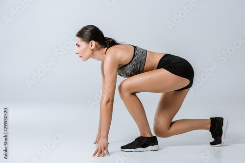 side view of brunette sportswoman training on grey