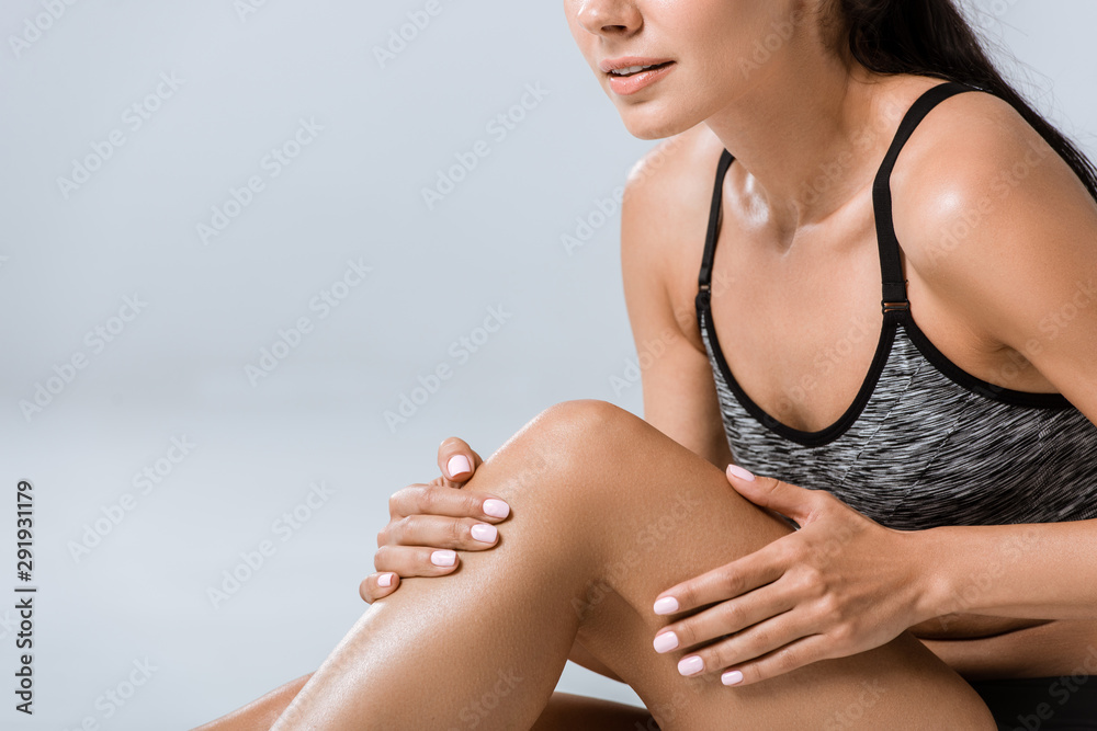 cropped view of sportswoman with knee pain on grey
