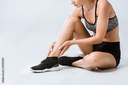 partial view of sportswoman with ankle pain on grey