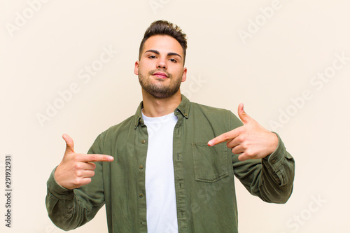 young hispanic man looking proud, arrogant, happy, surprised and satisfied, pointing to self, feeling like a winner against isolated background photo