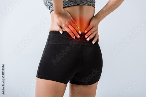 Photos partial view of sportswoman with lower back pain isolated on grey