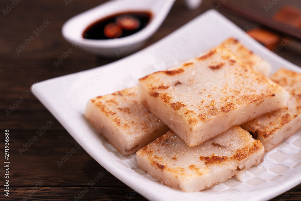 Delicious turnip cake, Chinese traditional local dish radish cake in restaurant with soy sauce and chopsticks, close up, copy space.