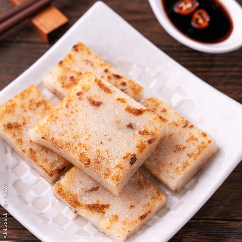 Delicious turnip cake, Chinese traditional local dish radish cake in restaurant with soy sauce and chopsticks, close up, copy space.