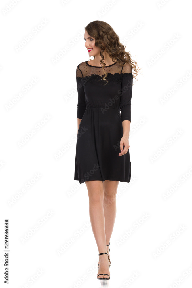 Young Woman In Elegant Black Dress And High Heels Is Walking And Looking Away. Front View. Young Woman In Elegant Black Dress And High Heels Is Walking And Looking Away. Front View.