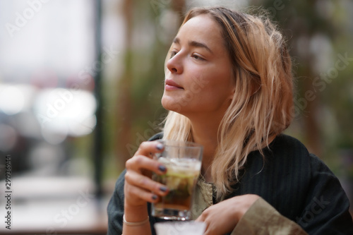 Attractive woman in her 20s with a glass cocktail or ice tea outside in sunlight