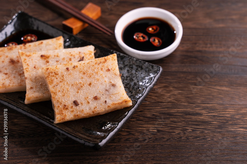 Delicious turnip cake, Chinese traditional local dish radish cake in restaurant with soy sauce and chopsticks, close up, copy space.